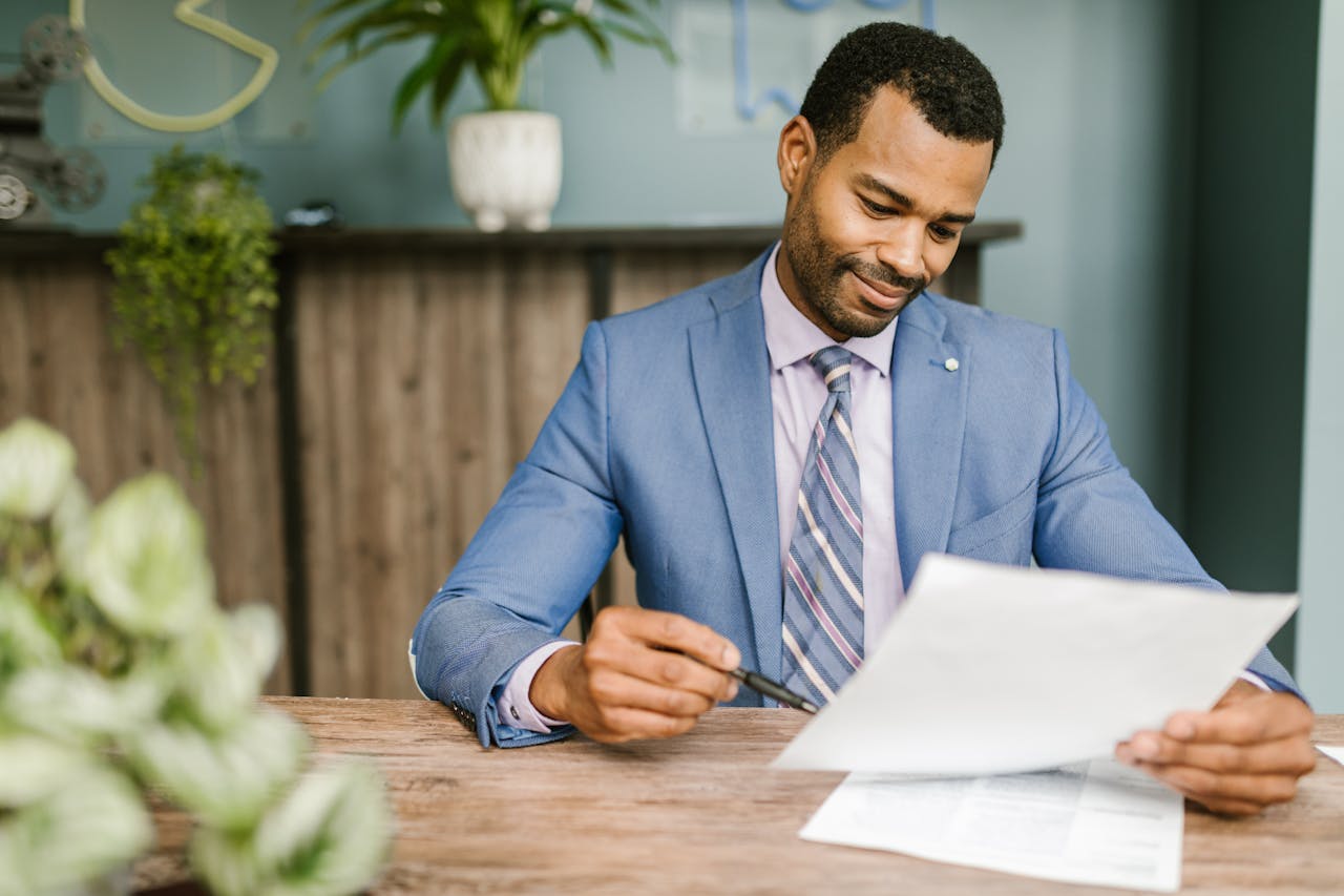 man-in-blue-suit-jacket-holding-white-paper-and-ballpen-7821514 Man in Blue Suit Jacket Holding White Paper and Ballpen